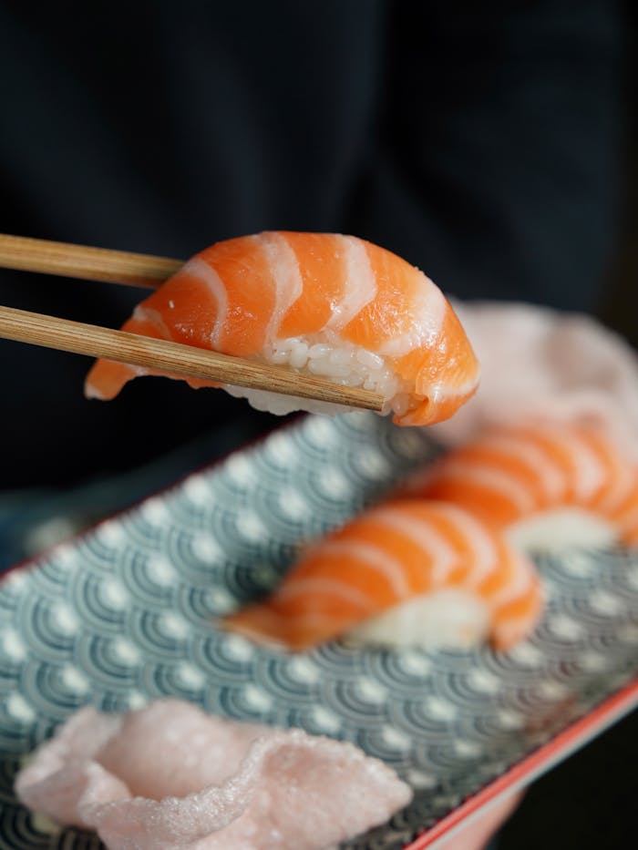 creative-03 A delicious salmon nigiri sushi held with chopsticks, showcasing traditional Japanese cuisine.