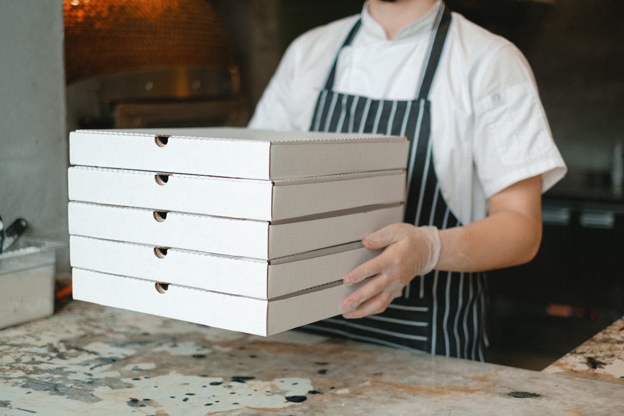 digital-01 Pizza deliveryman carrying stacked boxes in a restaurant kitchen setting.